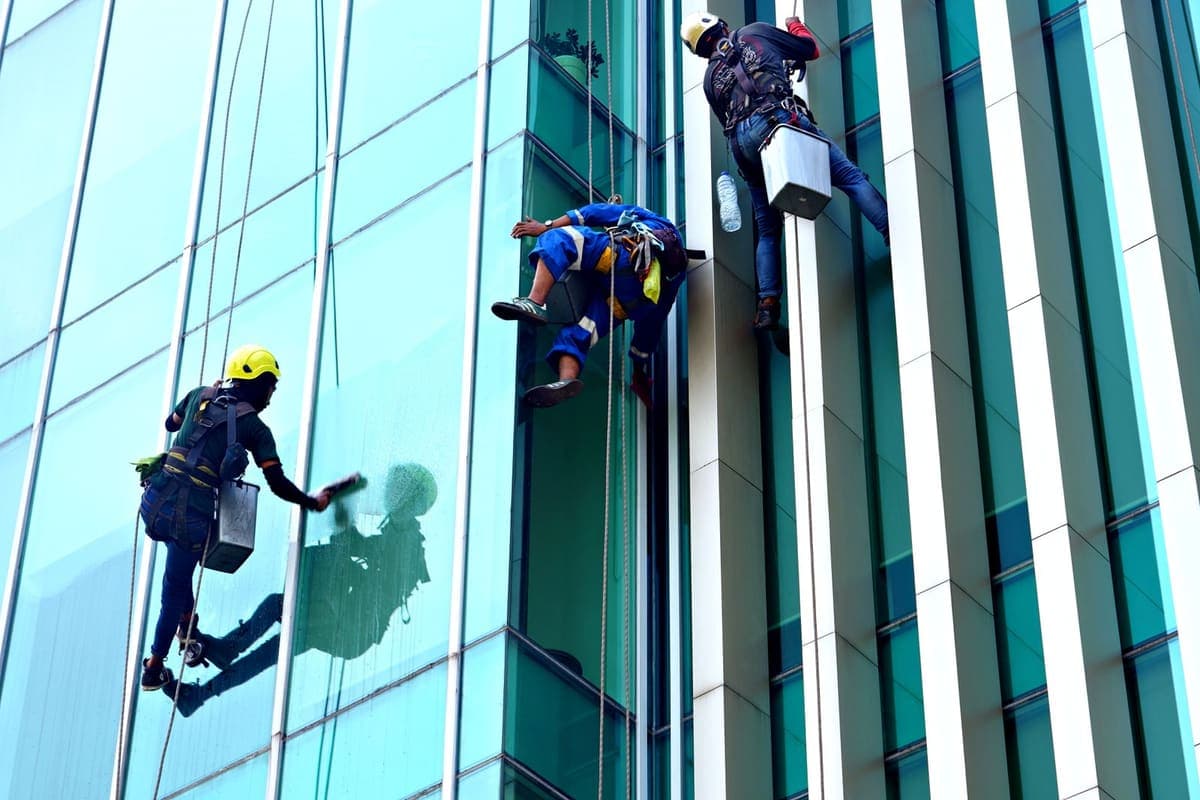 Equipe em trabalho de rapel na limpeza de uma fachada envidraçada